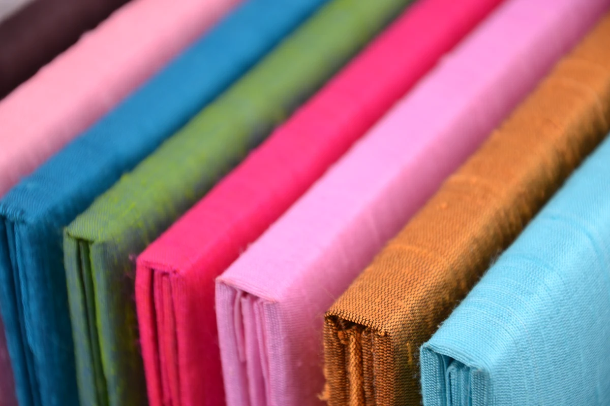 Finished dupioni silk book folios in pink, blue, green and gold, showing the woven texture and folded edges