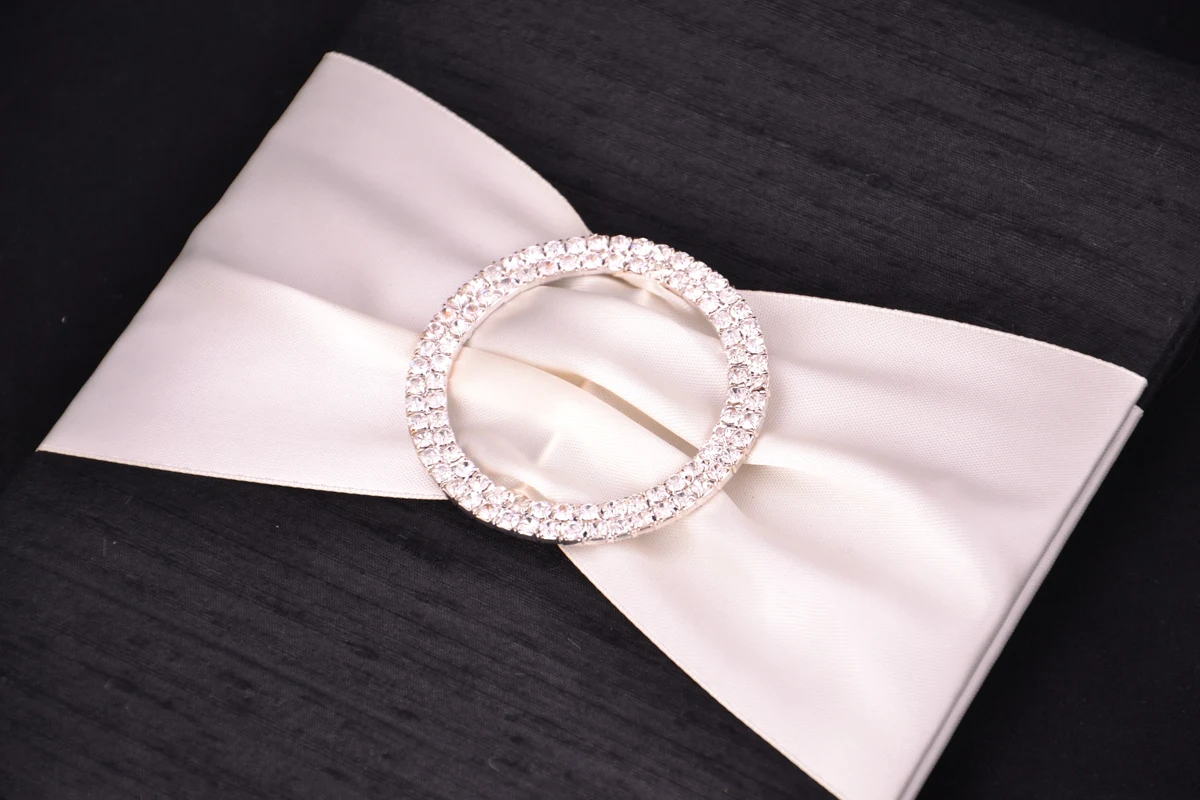 Ivory ribbon and a circular crystal embellishment against a dark invitation folio