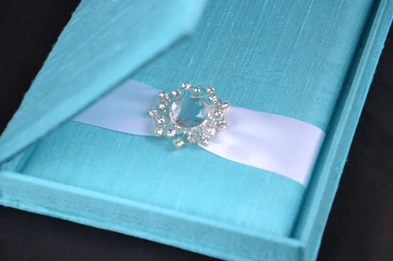 Aqua invitation box interior with pale ribbon and a floral jeweled buckle