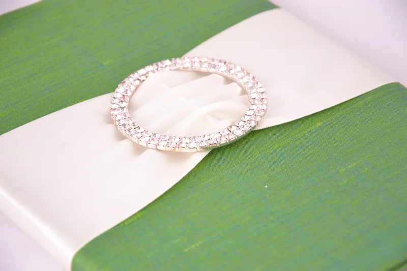 Close view of green invitation fabric, ivory ribbon and a circular jeweled buckle
