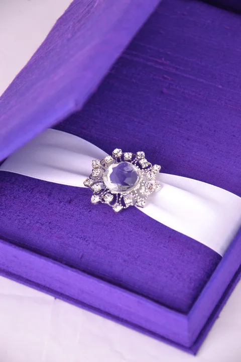 Open violet invitation box with a pale ribbon and jeweled embellishment