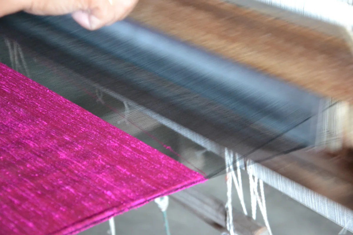 Close-up of magenta dupioni silk fabric being woven on a wooden loom