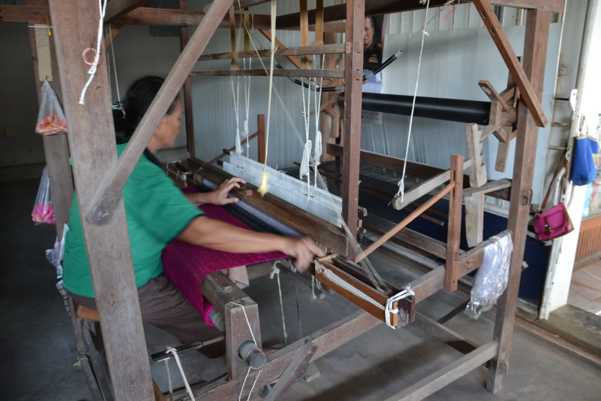Thai village artisan handweaving silk fabric on a traditional wooden loom