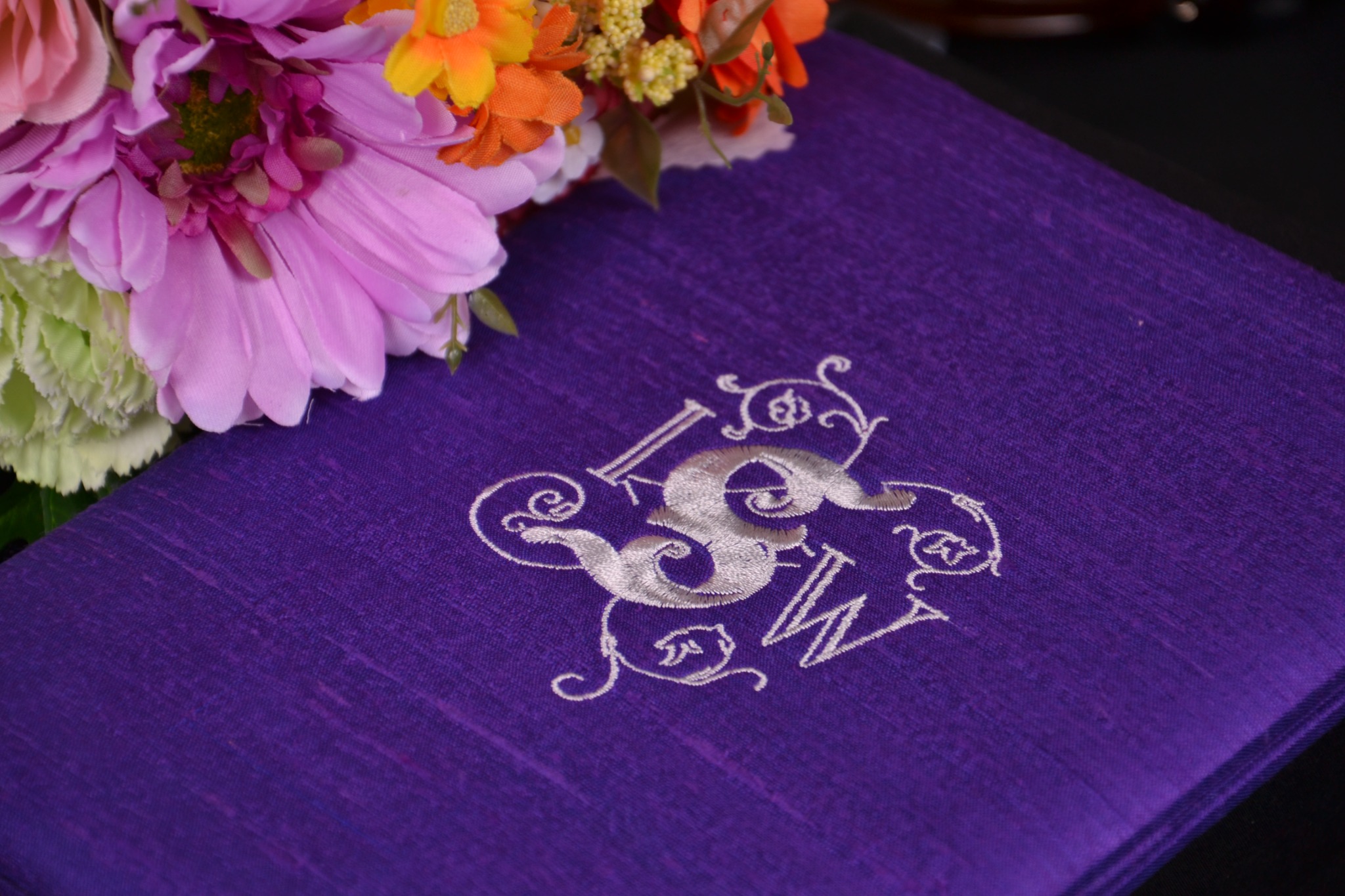 Purple handmade silk wedding invitation box with white custom embroidered monogram and wedding flowers